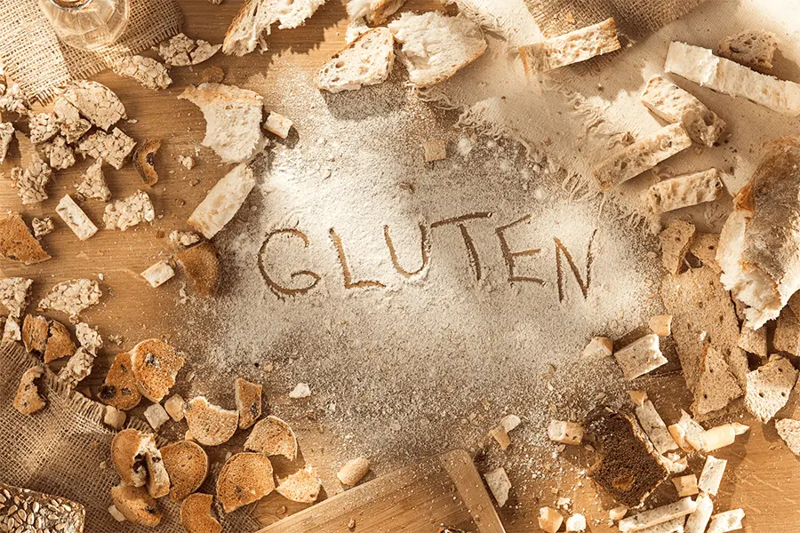 Pedazos de pan regados en una mesa con el texto gluten escrito en la harina regada en el centro