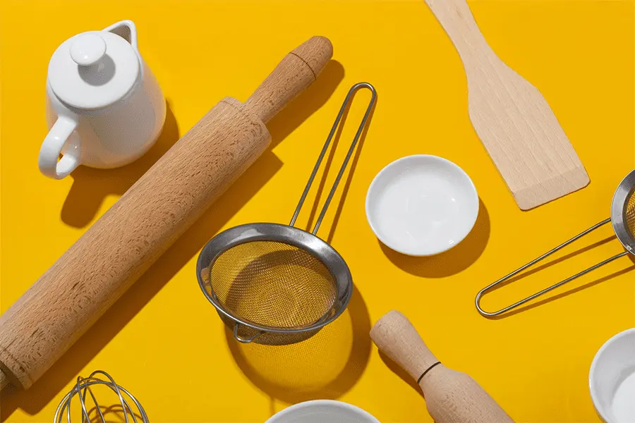 Rodillos y rasquetas sobre una mesa de color amarilla acompañadas de diversos utensilios