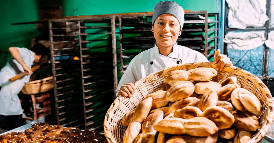 Mujer panadera mostrando una canasta repleta de bolillos