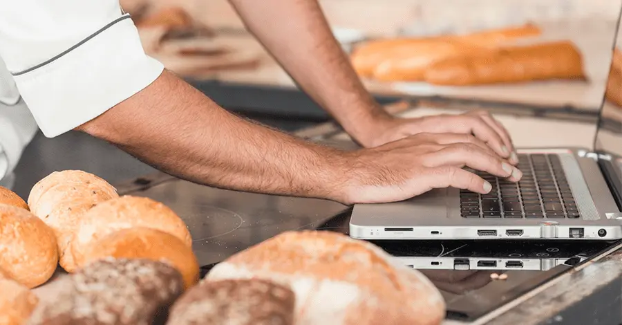 Panadero usando una laptop en la encimera de la cocina con panes
