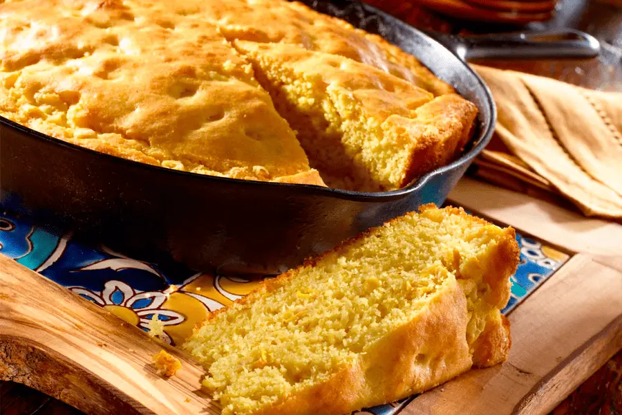 Pan de maíz en una charola siendo cortado en rebanadas en una mesa de cocina casera